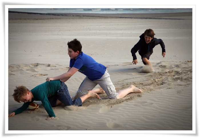 Drie jongens ravotten op het strand